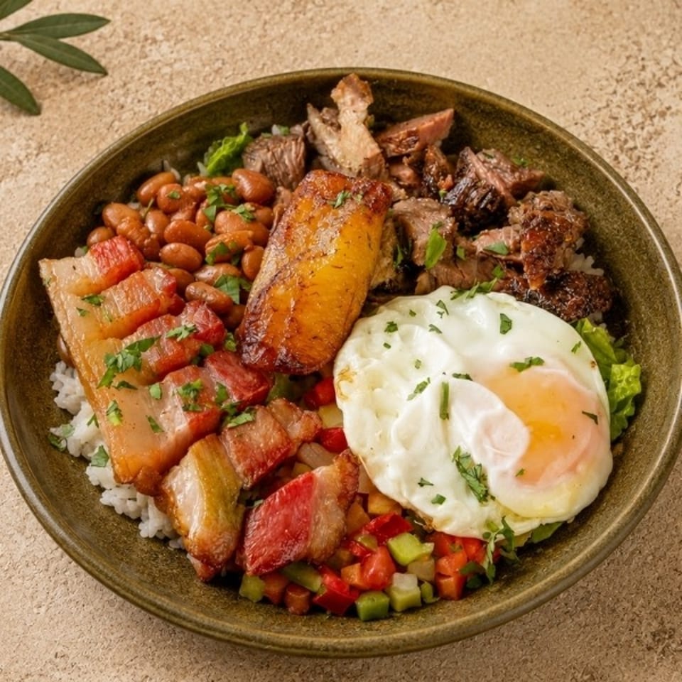 Bowl of rice topped with grilled meats, beans, roasted plantain, fried egg, bacon, and colorful diced vegetables.