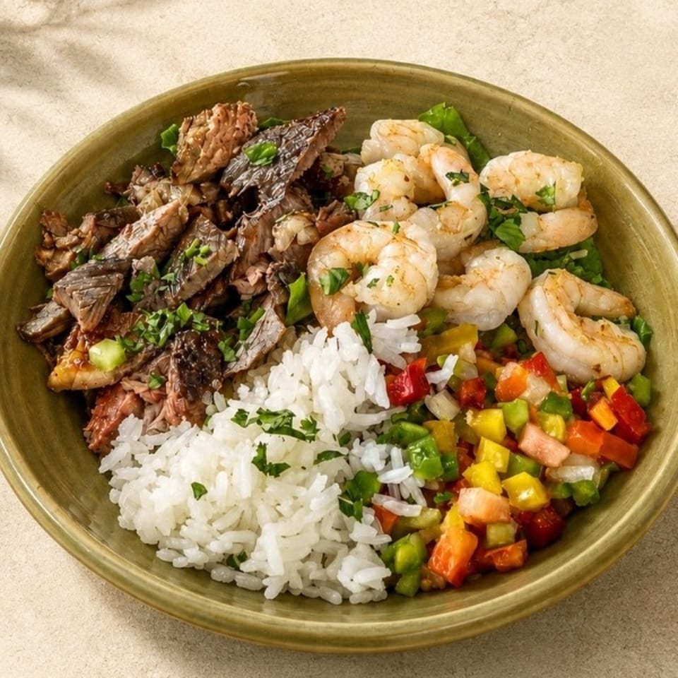 Bowl featuring grilled shrimp, shredded meat, white rice, and colorful diced vegetables garnished with fresh herbs.